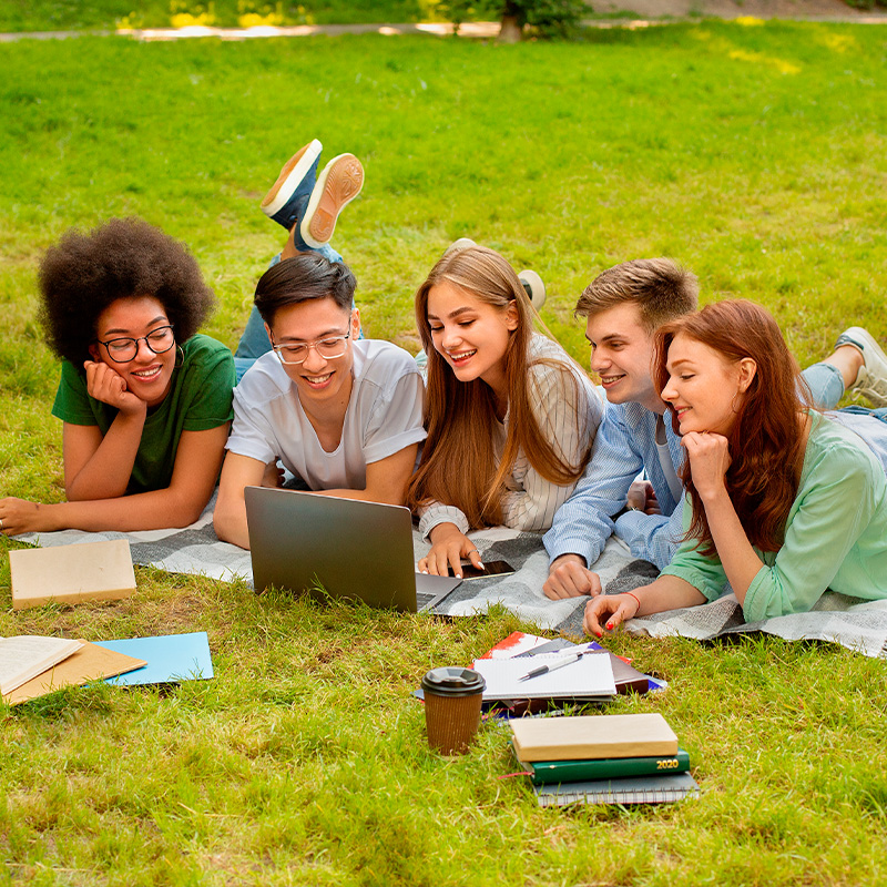 Students lying on grass looking at a laptop